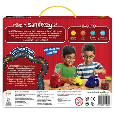 The back of the Sandeezy box features a red background with a description panel explaining the super sand’s texture and benefits, alongside icons for creative thinking, fine motor skills, process planning, and social communication. Two children build a red fire engine, yellow taxi, and blue ice-cream van using sand and accessories. A curved road graphic, sand tubs, manufacturing details, safety icons, and the Skillmatics website are shown at the bottom.