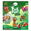 The Foil Fun Magnets “World of Animals” kit packaging features a glittery green background with colorful foil-decorated animal magnets including a dog, butterfly, giraffe, turtle, and lion. A child’s hand places the lion magnet on a metal surface inside a circular inset labeled “Works on all magnetic surfaces.” The box lists 20 foil sheets, 5 magnets, age range 4–12 years, and includes a warning for small parts.
