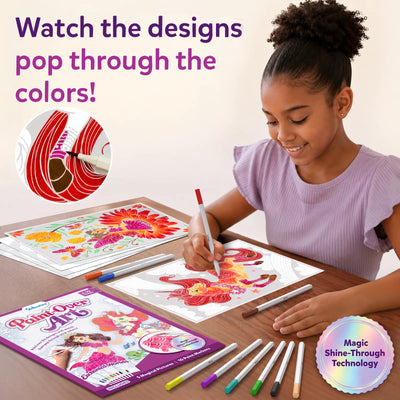 A young girl seated at a wooden table smiling while coloring Paint-Over Art sheets with markers; completed bright floral and fantasy designs visible, open kit box and scattered markers around, text reads Watch the designs pop through the colors, Magic Shine-Through badge shown.