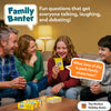 Family of four laughing on a couch playing Skillmatics Family Banter. A teenage girl in a red sweater holds up a yellow Family Banter card while parents and a teenage boy smile. The Family Banter box and card deck sit on the coffee table. An orange speech bubble shows the sample question: What time of day is peak family chaos hour. Text reads Fun questions that get everyone talking, laughing, and debating. The Perfect Holiday Game badge shown.