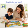 A smiling young child assembles the Skillmatics All About Wild Animals puzzle while an adult watches and encourages. The completed puzzle is spread across a table with loose puzzle pieces, six colorful learning boards and activity cards beside it. Suitable for ages 3–7.