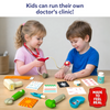 Two young children engage in imaginative doctor role-play using the Skillmatics Doctor Set. One child checks the other's blood pressure with a toy monitor while medical accessories, including a thermometer, syringe, pulse oximeter, bandages, prescription pad, medicine bottle, tray, and injury stickers, are spread across a table.