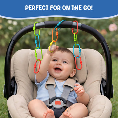 A baby seated in a padded stroller reaches upward to grasp colorful plastic Linkies attached along the curved stroller handle. The links appear in red, green, blue, yellow, and orange, hanging at different lengths. A blue banner at the top reads “Perfect for on the go,” illustrating how the links can be used as a portable activity during outdoor travel.