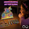 Lifestyle scene showing a child watching a glowing unicorn-and-candy Light-Up Sketcher artwork on a tabletop. Eight colorful Skillmatics markers and a reusable sticker sheet are nearby, while the illuminated drawing board glows in a dim room beside the Infinite Play logo.