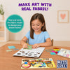 Young child seated at a table creating tactile fabric art with the Skillmatics Fab Tabs kit. Fabric pieces, picture boards, and activity materials are spread across the workspace as the child places textured fabric onto a design board, demonstrating the mess-free sensory craft experience.