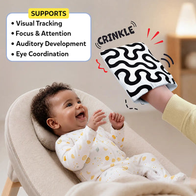 Skillmatics High Contrast Crinklers sensory scene showing a smiling infant in a cushioned baby rocker reaching toward a caregiver’s hand wearing a black-and-white wavy crinkle cloth marked CRINKLE. A SUPPORTS panel highlights visual tracking focus & attention, auditory development, eye coordination.