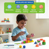 A young child happily plays with Brain Blocks at a table, stacking colorful geometric pieces and spheres into balanced structures. Above the child, icons and text highlight skill development areas including observation, critical thinking, problem solving, spatial reasoning, and fine motor skills. The scene emphasizes hands-on learning in a bright, child-friendly environment.