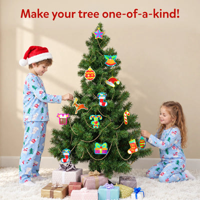 Children wearing festive pyjamas decorate a Christmas tree with colourful Skillmatics Foil Fun ornaments. The tree features handmade foil stars, stockings, bells, gifts and baubles, showcasing a creative holiday craft activity where children personalise decorations for display.
