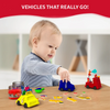 A toddler sits at a wooden table playing with bright kinetic-sand vehicles made from the Sandeezy kit, including a blue car, a yellow taxi, and a red fire engine topped with themed signs. In front of the child are scattered vehicle accessories like lights, cones, and labels. Jars of red and yellow sand sit nearby. A bold header above reads “Vehicles That Really Go!” against a red background.