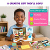 Smiling child holding a completed Fab Tabs room design board while seated at a table with fabric texture pieces and additional picture cards. A skills panel highlights fine motor development, creative thinking, and sensory exploration, presenting the activity as a gift for children ages 4 and up.