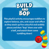 The Build And Bop logo appears at the top of a rounded blue text box on a light blue swirl background. The text explains that toddlers can explore balance, aim, and cause-and-effect by stacking five colourful, wobbly pieces and knocking them down with a soft ball. At the bottom right, an illustration shows the red Build And Bop ball beside a leaning stack of wobbly pieces, with motion lines indicating tipping.