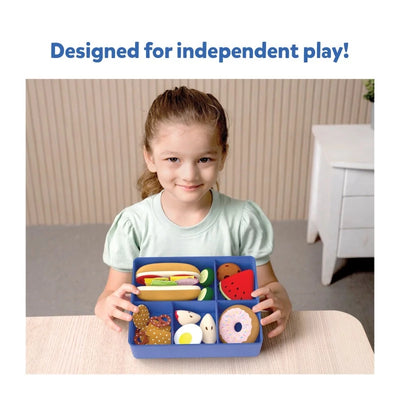 Young girl holding a blue toy bento box filled with pretend play food items