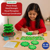 Child using the Skillmatics Poke-In Art Christmas Tree activity at a table, poking green fabric squares into a foam tree piece. A partly assembled tree, circular base, loose fabric squares, glitter sheets, golden star, mini gift boxes and poke-in sticks are visible, alongside listed skill benefits.