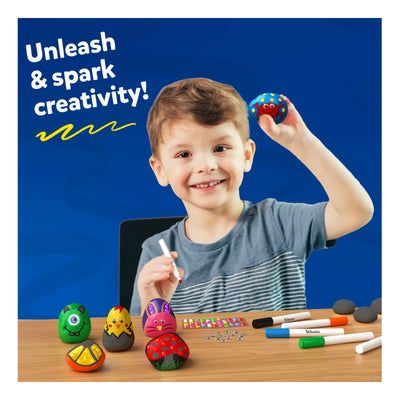 Boy smiling and holding a painted rock with decorated rocks and art supplies in the background